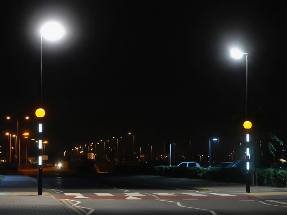 Midupost beacons at night on seperate sides of the road divided by a zebra crossing